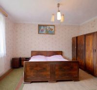 A bedroom in a family house with wooden furniture and a bed, wallpapered walls, and a floor with a wooden decor.
