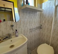 Bathroom with a mirror, sink, and toilet, tiled with light tiles.