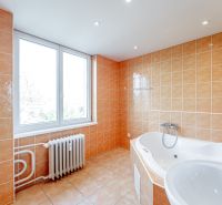A bathroom in a 2-room apartment with a corner bathtub, beige tiles, and a large window.