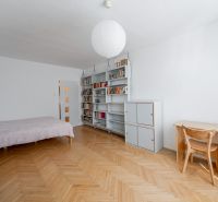 A room with a bed, bookshelf, table, and a floor with a wooden decor in a 2-room apartment.