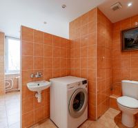 A bathroom in a 2-room apartment with a washing machine, toilet, and window, decorated in orange tones.