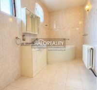 A bathroom in a family house with a bathtub, tiles, and white furniture.