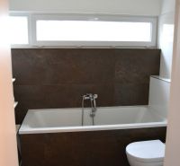 A bathroom in a family house with a bathtub, black tiles, and a bright window.
