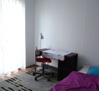 Bedroom in a family house with a desk, wooden decor flooring, and a bed.