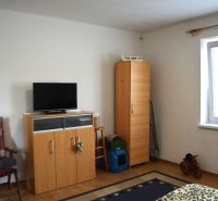 A room with furniture, a television, white walls, and a floor with a wooden decor.