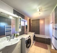 A bathroom in a family house with a washing machine, a bathtub, and tiled walls.