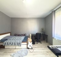 Bedroom in a family house with a bed, table, guitar, and keyboard, wooden decor flooring.