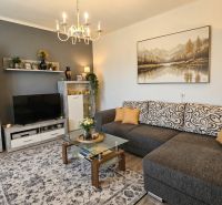 Living room in a family house with a comfortable couch, TV, decorations, and a wooden-patterned floor.