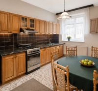 A kitchen with wooden cabinets and a table, tiled floor, refrigerator, gas stove.