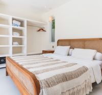 A bright bedroom interior in a villa with a wicker bed and white furniture.