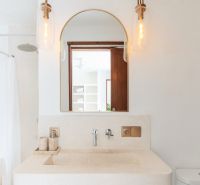 The bathroom of the villa with a round mirror, lights, and a natural stone sink.