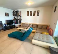 Living room in a family house with a tiled stove, sofa, and shelves on the wall.