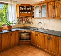 A kitchen in a family house with wooden cabinets, a black countertop, and a ceramic sink.