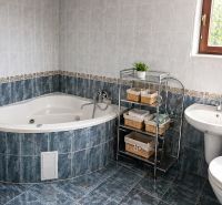 A bathroom in a family house with a corner bathtub and a sink, tiled with ceramic tiles.