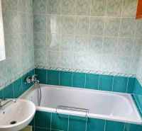 A bathroom in a family house with a bathtub, a sink, a window, and ceramic tiles.