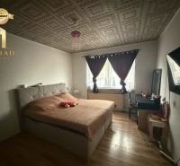 A bedroom in a family house with a wooden decor floor, a bed, and a table.