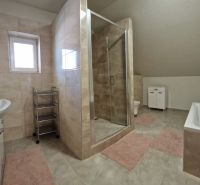 A bathroom in a family house with a bathtub, shower, and tiles in neutral tones.