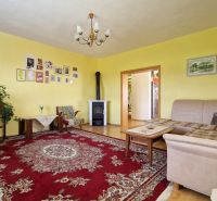 Living room with a beige sofa, red carpet, and wood-patterned flooring in a family house.
