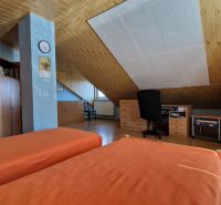 A room in a family house with orange beds, a slanted ceiling, and wooden furniture.