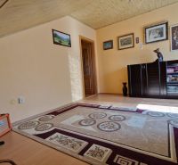 A room in a family house with a carpet, a floor with a wooden decor, and a guitar in the corner.