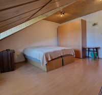 Attic bedroom in a family house with a wooden decor floor and simple furnishings.