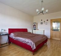 A bedroom in a family house with a red bed and a wooden decor floor.