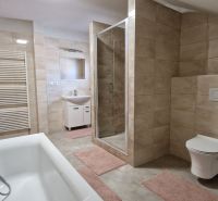 A bathroom in a family house with a bathtub, a shower corner, and beige tiles.