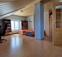 Attic room of a family house with a desk, sofa, and wooden decor flooring.