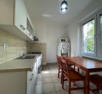 A kitchen in a 2-room apartment with a dining table, white cabinets, and tiles.