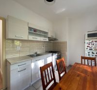 A kitchen in a 2-room apartment with a white kitchen unit and a wooden table.
