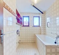 A bathroom in a family house with windows, a bathtub, and tiled walls.