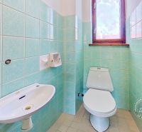 A toilet with a sink and green tiles in a family house.