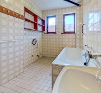 A bathroom in a family house with subtle tile patterns and two windows.