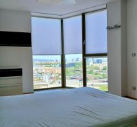 A bright bedroom in a 2-room apartment with a view of the city from large windows.