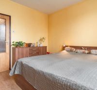 A bright bedroom with a bed, shelf, and wood-decor flooring in a 3-room apartment.
