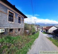 A street in Heľpa with traditional houses surrounded by nature and mountains on the horizon.