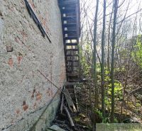 Dilapidated stairs by the wall of Unusual Properties in Heľpa, surrounded by plants and shrubs.