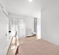 A bright bedroom with wood-patterned flooring and simple furniture in a 2-room apartment.