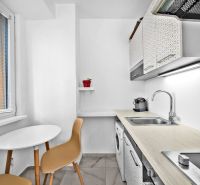 A kitchen of a 2-room apartment with a window, white furniture, and a table with chairs.