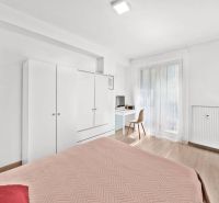 Bedroom in a two-room apartment with white furniture and a wood-patterned floor.
