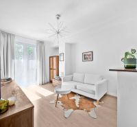 A bright living room in a two-room apartment with wood-patterned flooring and a white sofa.