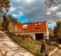 Cottage on Recreation Area Street in Nova Kelca, surrounded by forest trees and a road.
