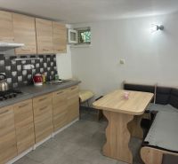 A kitchen in a cottage with a stove, wooden cabinets, and a corner bench.