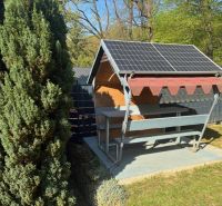 A cottage in Ilava with a gazebo and a solar panel in a garden surrounded by trees.