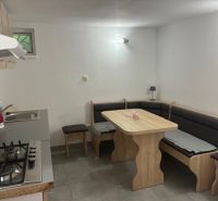 A kitchen in a cottage with a corner bench, table, and cooktop.
