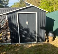 A garden with a tin shed in Ilava, next to which firewood is stored.