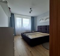 A bedroom with a gray bed, curtains, and a wooden decor floor in a 3-room apartment.