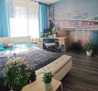 A bedroom in a 3-room apartment with a wooden decor floor and a city photo wallpaper.