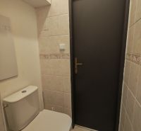 A toilet in a 3-room apartment with light tiles and a white toilet.