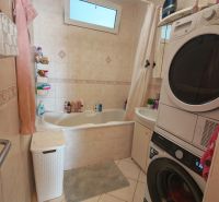 Bathroom with a washing machine in a 3-room apartment, with a bathtub and a window, tiled floor.